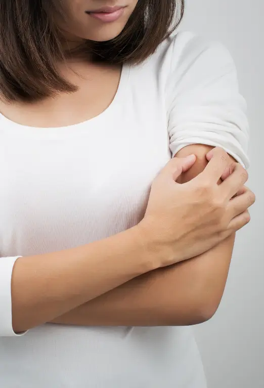 Woman scratching an itchy arm due to a skin allergy before receiving homeopathic treatment at Dr. L Square Homeopathy Clinic in Kolaghat.